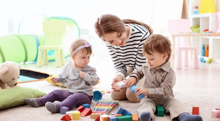 Young nanny playing with little children, indoors