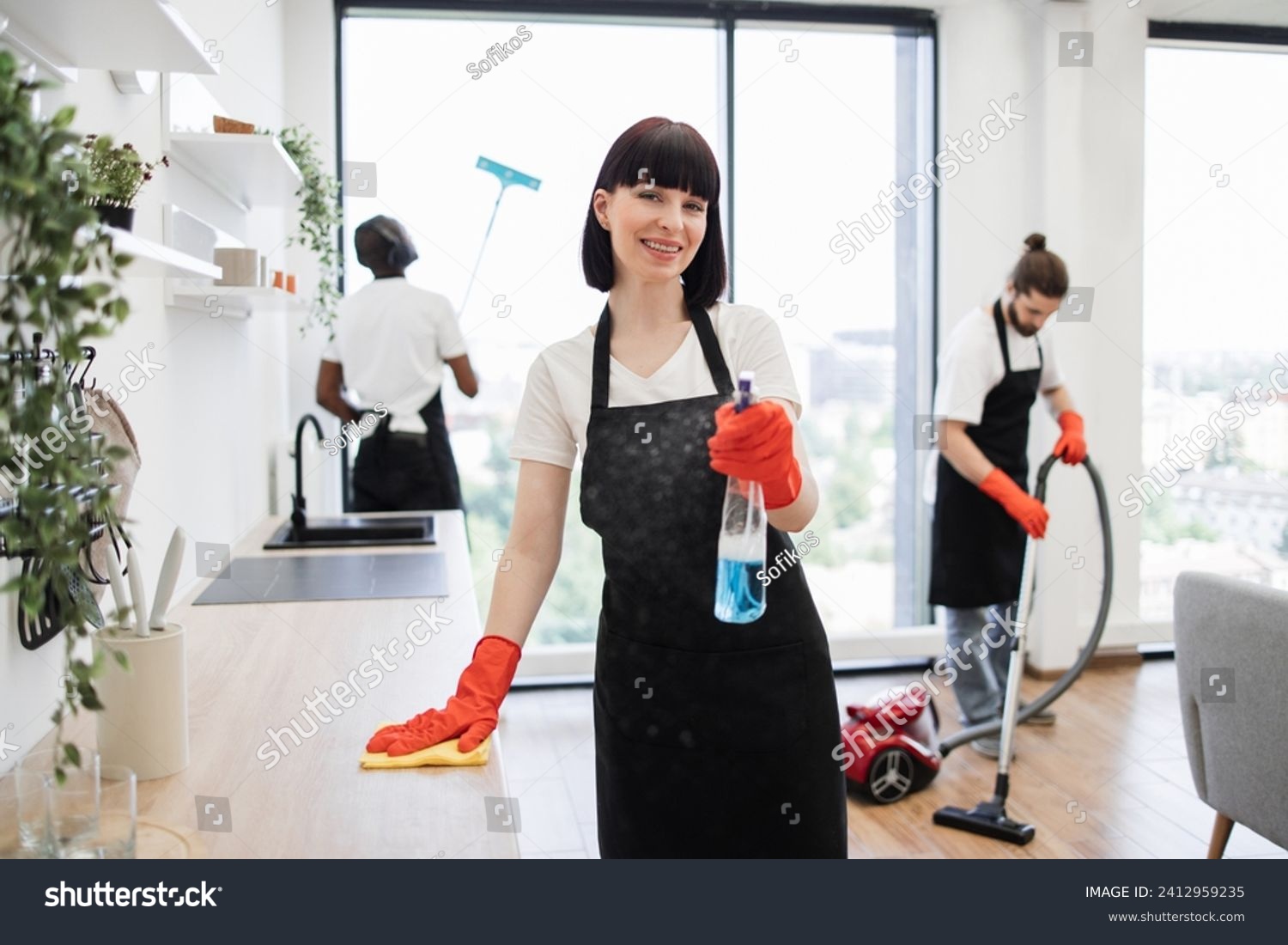 stock-photo-caucasian-janitor-in-apron-and-gloves-having-fun-sprays-detergent-into-camera-while-cleaning-table-2412959235